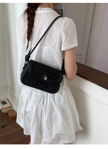 Détail du sac à bandoulière à nœud noir avec pendentif cœur et texture à pois