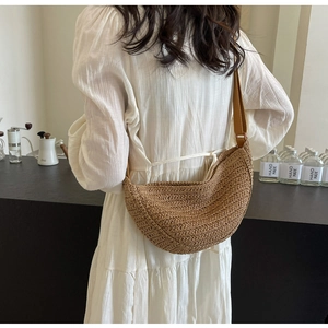Borsa a tracolla in paglia marrone intrecciata a mano in un caffè con abito minimalista