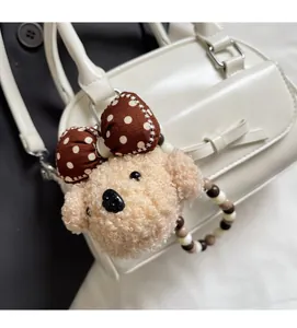 Detail of plush dog keychain with polka dot bow and beaded ring on a white handbag