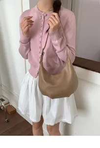 Detail view of khaki brown crescent shoulder bag styled with pink cardigan and pleated skirt