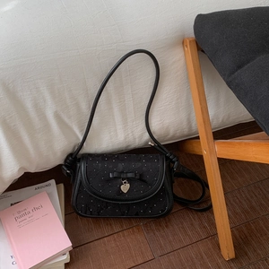 Détail du sac à bandoulière noir avec nœud en dentelle florale et pendentif cœur sur bois