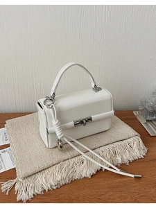 Detailansicht einer weißen Ledertasche mit silbernem Drehverschluss und Seildekoration