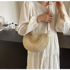 Modella indossa una borsa a mezzaluna in paglia beige con tracolla in un caffè moderno