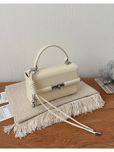 Detailansicht der cremefarbenen Handtasche mit Silberschloss auf einer Webmatte