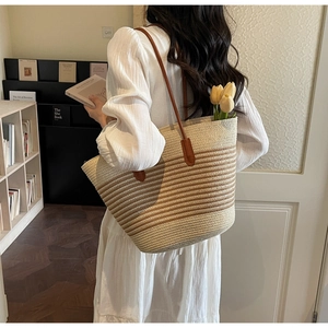 Close-up of woven straw tote bag with gradient stripes and slender brown leather straps