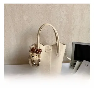Detail of off-white lychee grain leather bucket bag with cute plush bear charm