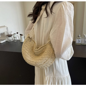 Dettaglio di una borsa a tracolla in paglia intrecciata beige con trama naturale su modella