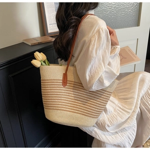 Close-up of a large striped straw tote bag with brown leather straps for summer travel