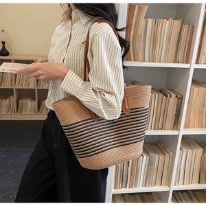 Detail showing the straw tote bag with black stripes and long brown leather shoulder strap