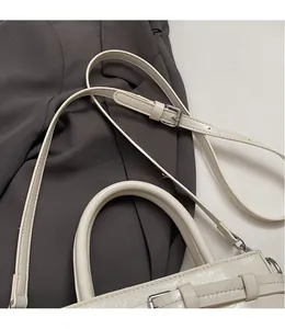 Close-up of beige leather bag featuring thick cylindrical handle and adjustable strap