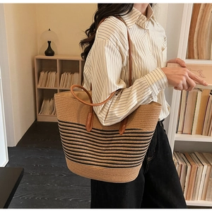 Detail of large woven straw tote with black stripes and brown leather straps on shoulder