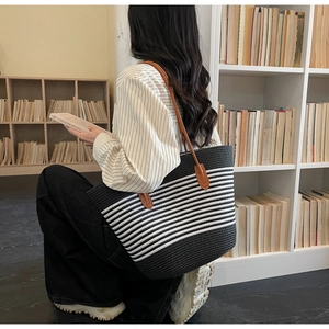 Detail of striped woven straw tote bag with brown leather shoulder straps and large capacity