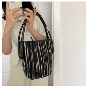 Detail view of striped woven bucket bag with black leather handle and silver hardware