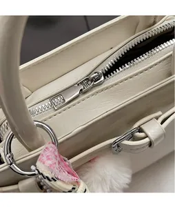 Close-up of silver metal zipper pull and textured leather on a cream crossbody bag