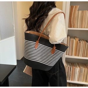 Detail of a large striped straw tote bag with brown leather handles worn by a model