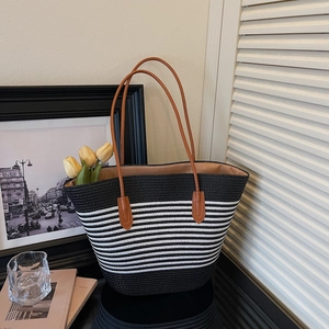Detailed close-up of woven straw tote bag with black and white stripes and brown straps