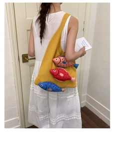 Détail du sac en tricot jaune avec poupées poissons 3D porté sur une robe en dentelle blanche