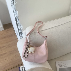 Sac hobo rose en demi-lune avec pendentif nain mignon sur un fond de canapé beige