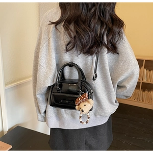 Detail of glossy black bow bag with a cute brown plush bear charm and beaded accessory