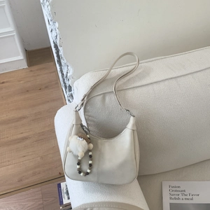 Détail d'un sac hobo en cuir crème avec breloque mouton et chaîne perlée sur un canapé