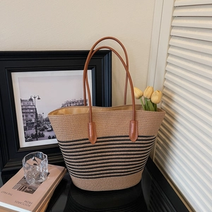 Detail of khaki woven straw tote bag with black stripes and brown leather handles