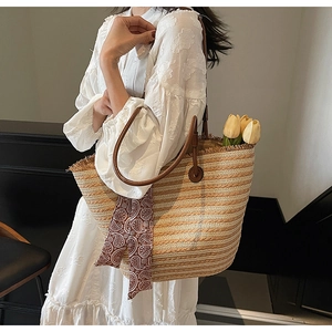 Detail of straw woven tote bag featuring brown leather straps and vintage silk scarf accent