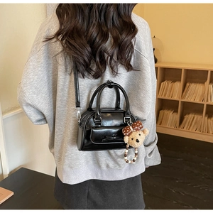Black glossy bow handbag detail with a cute plush bear pendant shown on shoulder