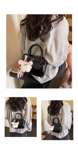 Detail view of a black glossy handbag with a cute white bunny keychain and shoulder strap
