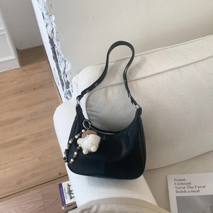Détail du sac hobo noir avec pendentif peluche et breloque perlée sur un canapé blanc