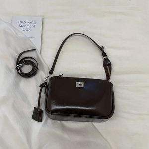 Detail of dark brown glossy patent leather baguette bag with silver turn-lock and straps