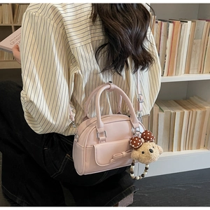 Detail of light pink Boston bag featuring a bow pocket and cute plush bear keychain