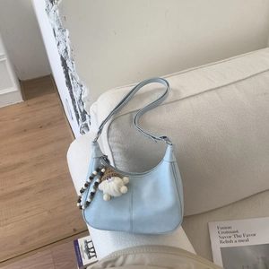 Détail du sac croissant bleu clair avec pendentif en peluche sur un canapé blanc