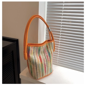 Detail of colorful striped canvas bucket bag featuring orange leather handle and metal buckle