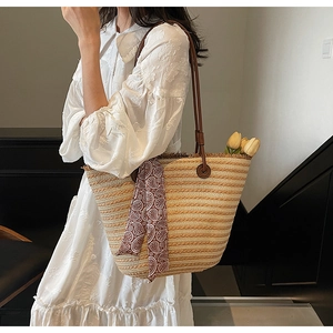 Close-up of woven straw tote bag featuring leather handles and a floral silk scarf detail