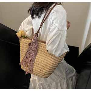 Detail of straw tote bag featuring woven texture, silk scarf, and brown leather handles