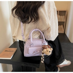 Detail of light purple bow-knot mini bag with soft plush bear charm in a cozy indoor setting