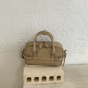 Détail du sac bowling en cuir beige avec boucles argentées sur socle en pierre