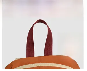 Detailed close-up of heavy-duty dark red webbing handle and orange nylon backpack seams