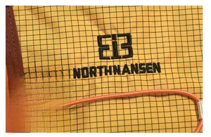 Detail of tear-resistant yellow fabric with black embroidered logo and orange cord