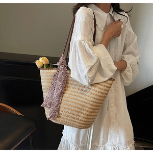 Detail of hand-woven straw tote with brown leather strap and decorative silk scarf