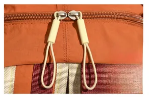 Close-up of dual metal zippers with beige pull cords on a bright orange nylon backpack