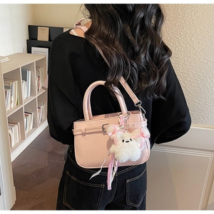 Pink crossbody square bag with a plush puppy charm shown on a shoulder strap