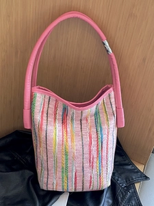 Pink striped woven bucket bag with vibrant vertical patterns and a faux leather strap