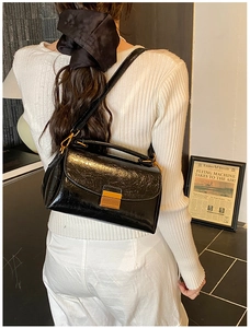 Détail d'un sac à main en cuir noir brillant avec une boucle métallique dorée