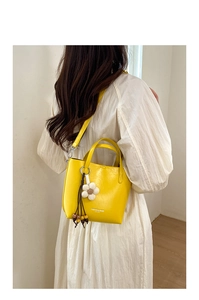 Detailed view of yellow bucket bag with floral charm and wooden bead tassel accessory