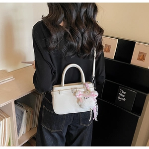 Chic off-white gloss PU leather crossbody bag with a cute plush bear charm on a model