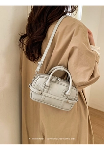 Détail du sac Boston gris clair avec sangles à boucle porté sur un trench-coat