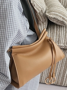 Minimalist camel leather crossbody bag with drawstring metal rings on a casual shoulder strap