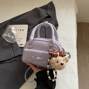 Detail of lilac purple handbag with bow decor, front pocket and cute teddy bear charm
