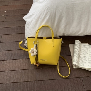 Detail of yellow bucket bag with floral charm and leather strap on wooden floor